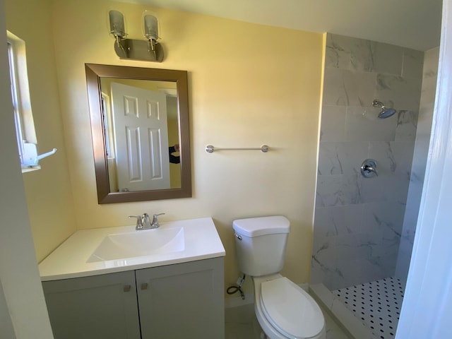 bathroom with toilet, tiled shower, and vanity