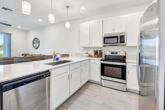 kitchen featuring hanging light fixtures, appliances with stainless steel finishes, sink, and white cabinets