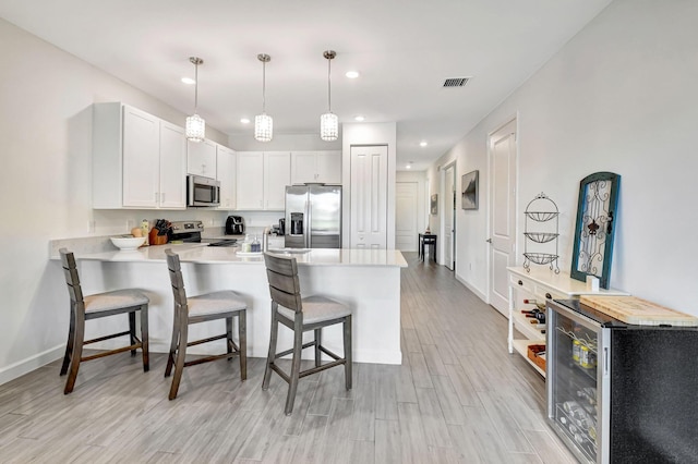 kitchen with appliances with stainless steel finishes, wine cooler, white cabinets, a kitchen breakfast bar, and kitchen peninsula