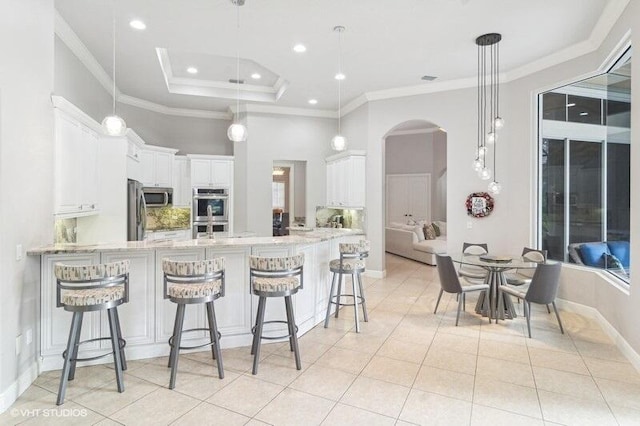 kitchen with pendant lighting, appliances with stainless steel finishes, white cabinetry, light stone counters, and kitchen peninsula