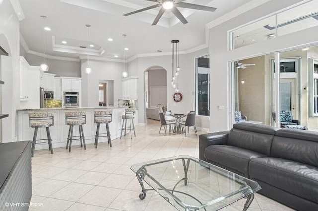 living room featuring crown molding, light tile patterned floors, a tray ceiling, ceiling fan, and a high ceiling