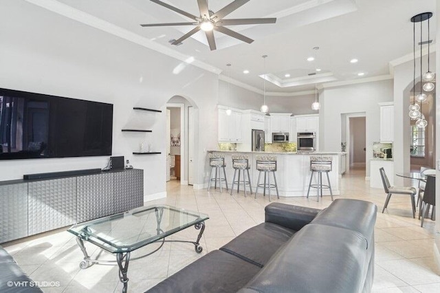 living room with crown molding, a raised ceiling, a high ceiling, and light tile patterned floors