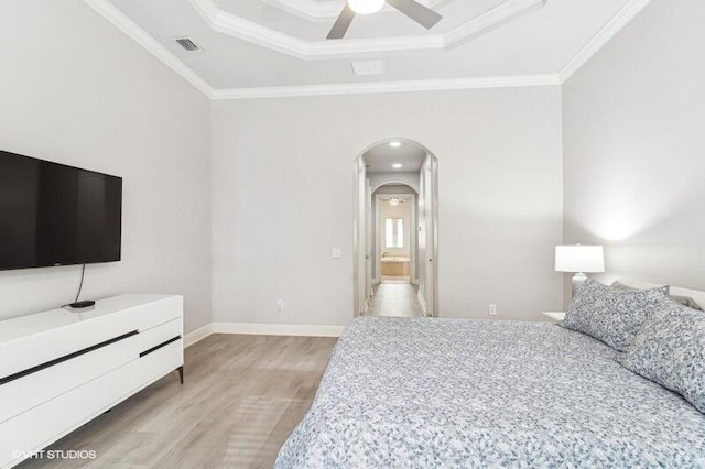 bedroom with ensuite bathroom, crown molding, light hardwood / wood-style flooring, a tray ceiling, and ceiling fan