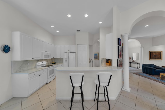 kitchen with a kitchen bar, kitchen peninsula, white appliances, decorative columns, and white cabinets