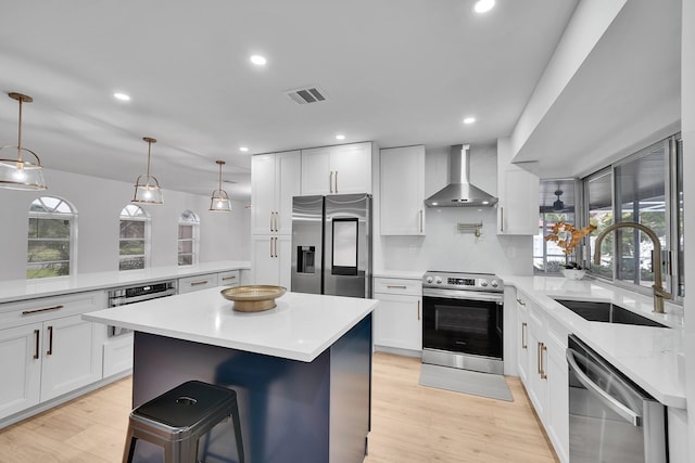 kitchen with a kitchen island, visible vents, a sink, wall chimney range hood, and appliances with stainless steel finishes