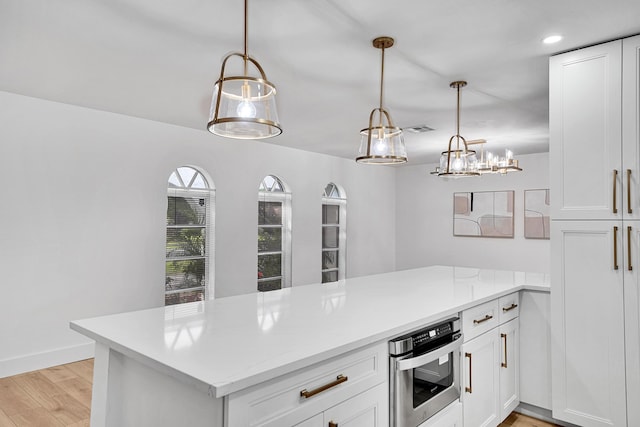 kitchen with hanging light fixtures, white cabinets, oven, and light hardwood / wood-style flooring