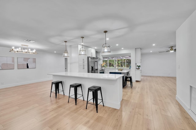 kitchen featuring light wood-type flooring, a breakfast bar area, white cabinetry, and hanging light fixtures