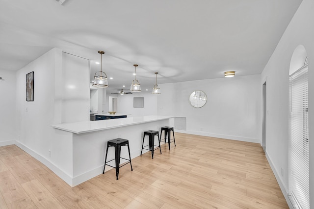 kitchen with pendant lighting, a kitchen bar, kitchen peninsula, and light hardwood / wood-style floors