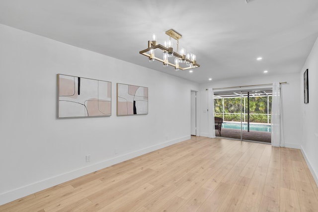 spare room featuring an inviting chandelier and light wood-type flooring