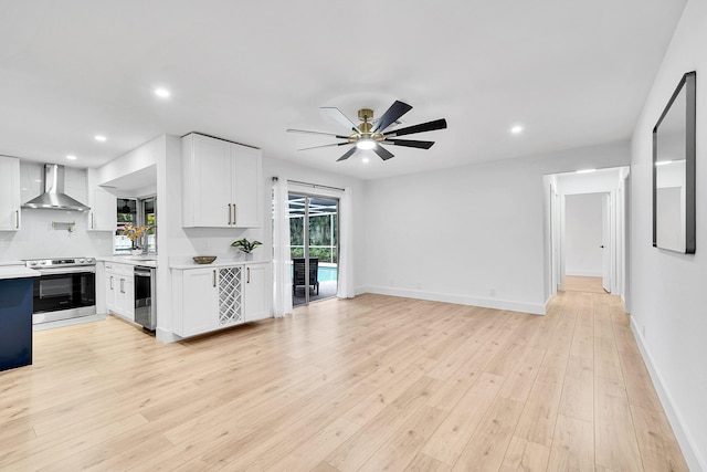 kitchen featuring stainless steel electric stove, light hardwood / wood-style floors, white cabinets, and wall chimney range hood