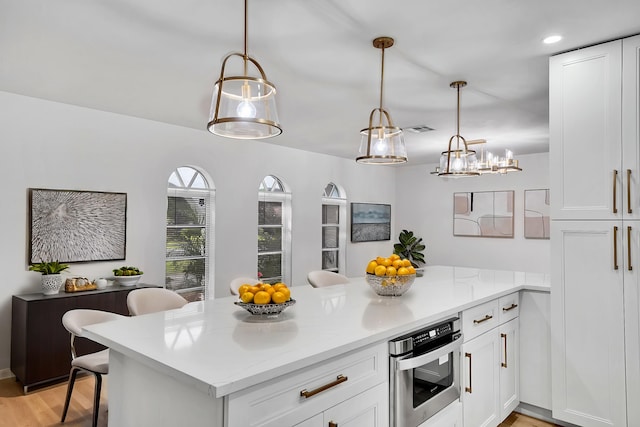 kitchen featuring pendant lighting, white cabinets, stainless steel oven, and a peninsula