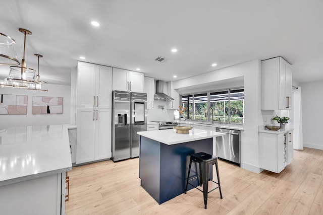 kitchen with wall chimney range hood, light countertops, a kitchen breakfast bar, appliances with stainless steel finishes, and a sink