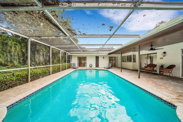 view of swimming pool with ceiling fan, glass enclosure, and a patio area