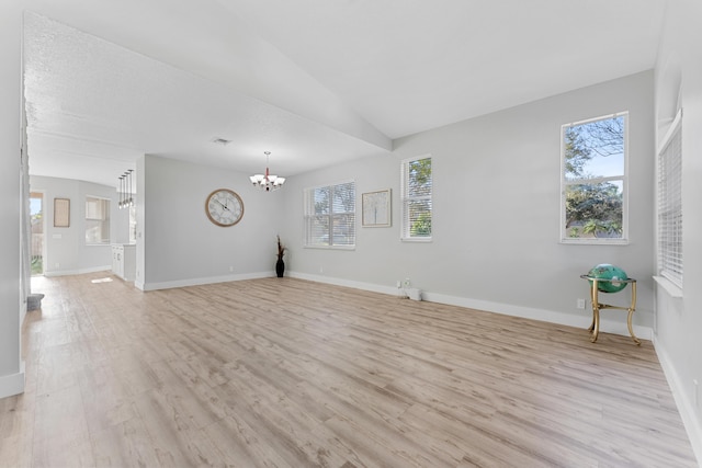 unfurnished living room featuring vaulted ceiling, a chandelier, and light hardwood / wood-style flooring