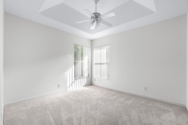 spare room with light colored carpet, ceiling fan, and a raised ceiling