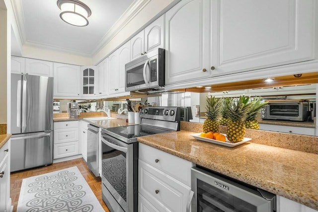 kitchen featuring stainless steel appliances, beverage cooler, light stone countertops, ornamental molding, and white cabinets