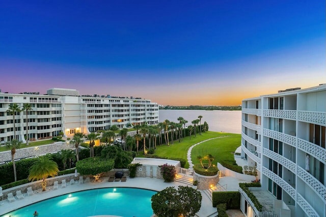 pool at dusk with a water view, a patio, and a yard