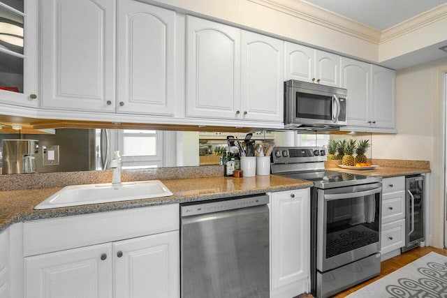 kitchen with appliances with stainless steel finishes, beverage cooler, white cabinetry, sink, and ornamental molding