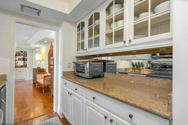 kitchen with stainless steel range with electric stovetop, light parquet flooring, ornamental molding, white cabinets, and light stone counters