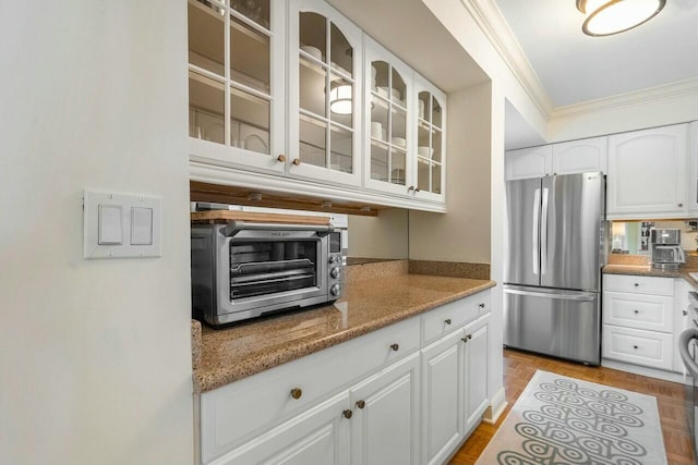 kitchen featuring stainless steel refrigerator, crown molding, light parquet floors, light stone countertops, and white cabinets