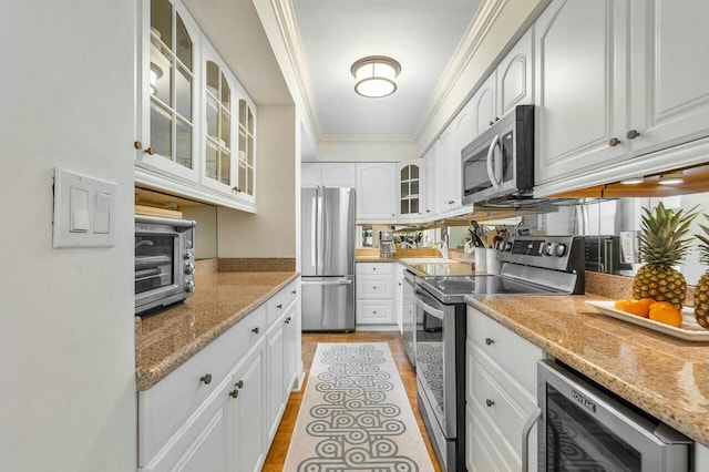 kitchen with appliances with stainless steel finishes, white cabinetry, wine cooler, light stone counters, and crown molding