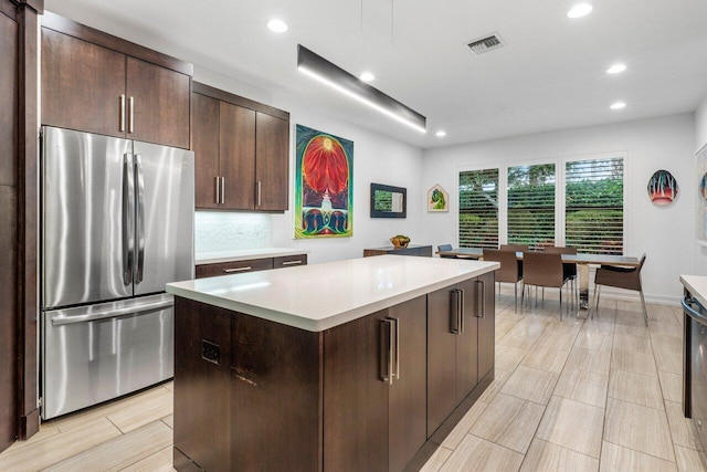 kitchen featuring stainless steel refrigerator, dark brown cabinets, decorative backsplash, and a kitchen island