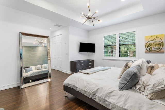 bedroom with a closet, dark hardwood / wood-style floors, a chandelier, and a tray ceiling