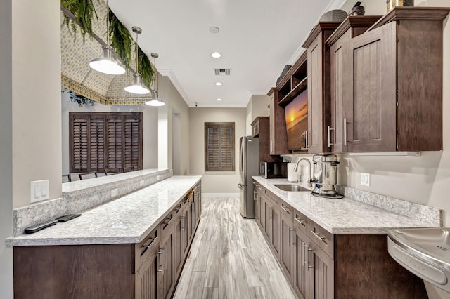 kitchen with pendant lighting, sink, crown molding, appliances with stainless steel finishes, and light hardwood / wood-style floors