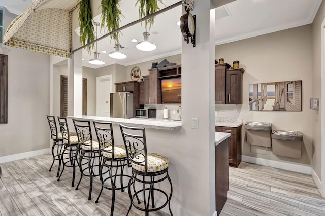 kitchen featuring crown molding, appliances with stainless steel finishes, a breakfast bar area, and dark brown cabinets