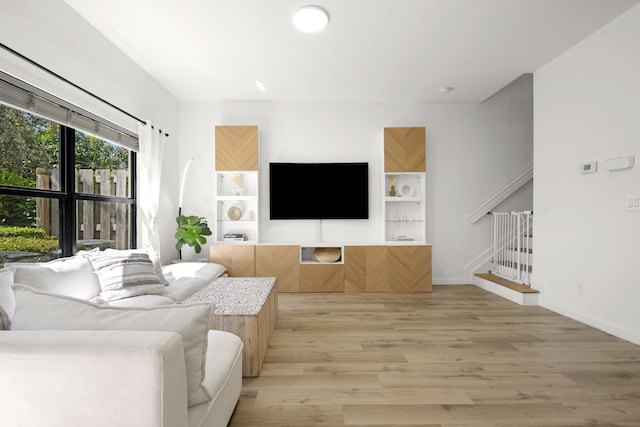 living room with light wood-type flooring, baseboards, and stairway