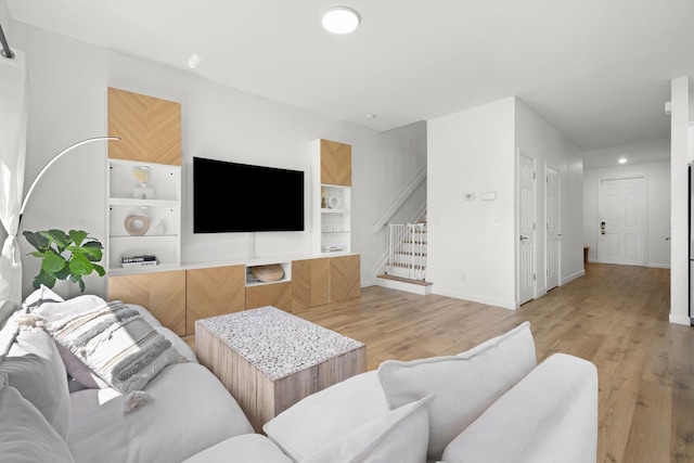 living room with stairway, built in shelves, baseboards, and light wood-style floors