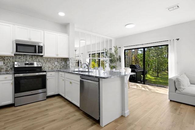 kitchen with light stone counters, visible vents, a peninsula, stainless steel appliances, and decorative backsplash