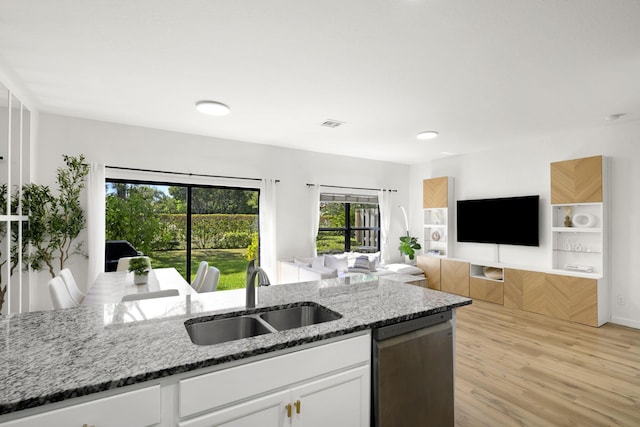 kitchen with light wood-style flooring, a sink, stone countertops, white cabinetry, and dishwasher