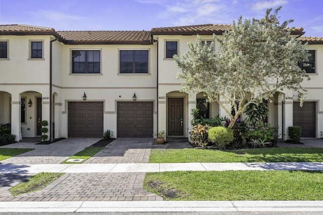 multi unit property with a tiled roof, decorative driveway, a garage, and stucco siding