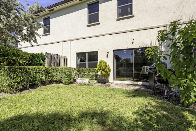 back of house with a tiled roof, a lawn, and stucco siding