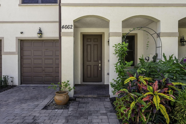 view of exterior entry featuring stucco siding, decorative driveway, and a garage