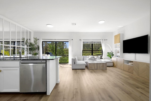 kitchen featuring light wood-type flooring, stainless steel dishwasher, open floor plan, white cabinetry, and dark stone counters