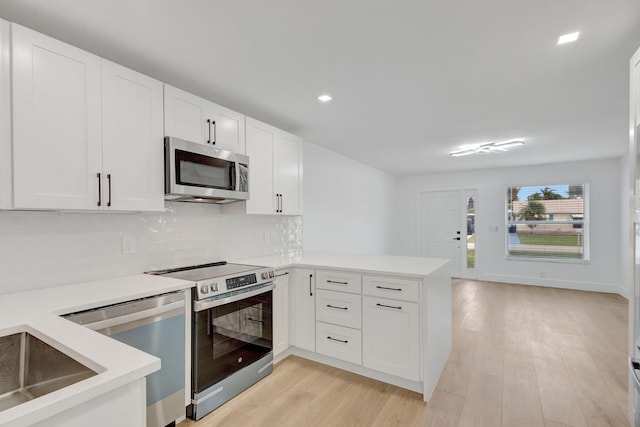 kitchen with light hardwood / wood-style flooring, stainless steel appliances, white cabinets, decorative backsplash, and kitchen peninsula