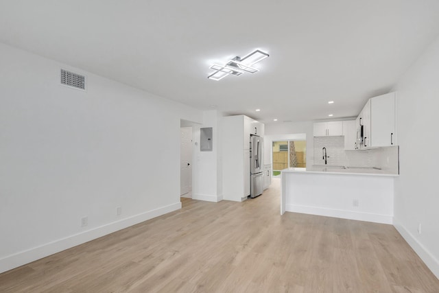 unfurnished living room with sink, electric panel, and light wood-type flooring