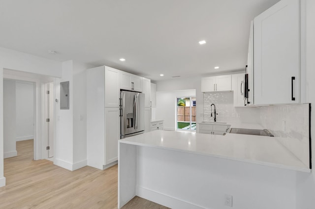 kitchen with stainless steel refrigerator with ice dispenser, white cabinetry, light hardwood / wood-style flooring, electric panel, and kitchen peninsula