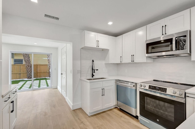 kitchen featuring sink, appliances with stainless steel finishes, backsplash, light hardwood / wood-style floors, and white cabinets