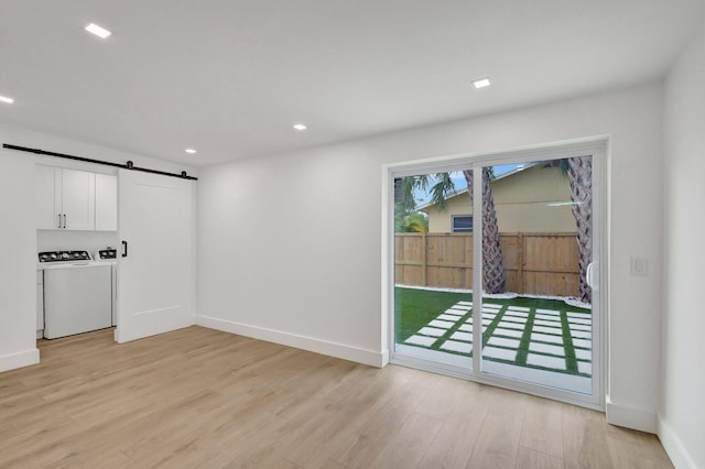 interior space featuring washing machine and dryer, a barn door, and light hardwood / wood-style flooring