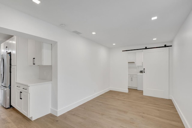 unfurnished room featuring a barn door, washer / clothes dryer, and light hardwood / wood-style flooring