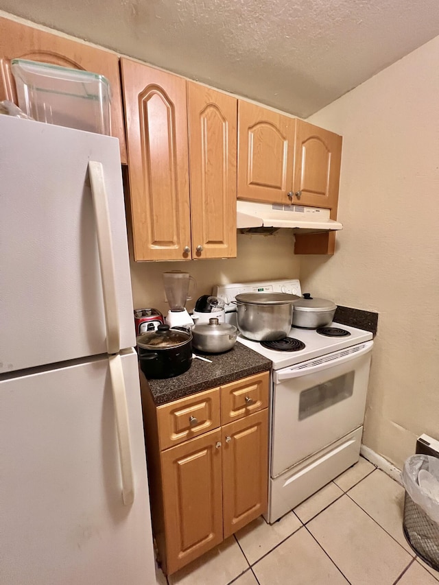 kitchen with white appliances, light brown cabinets, a textured ceiling, and light tile patterned flooring