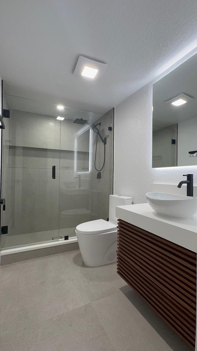 bathroom featuring a textured ceiling, toilet, walk in shower, and vanity