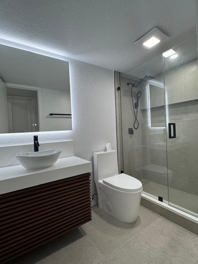 bathroom featuring toilet, vanity, a shower with shower door, and a textured ceiling