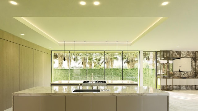 interior space with pendant lighting, sink, light stone counters, and a raised ceiling