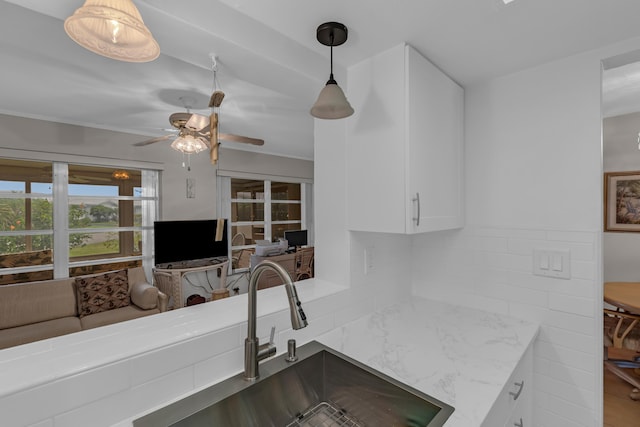 kitchen featuring pendant lighting, sink, ceiling fan, white cabinetry, and light stone countertops