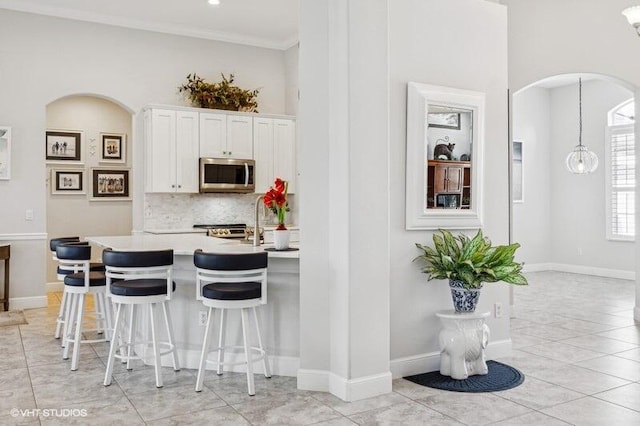 kitchen with light tile patterned flooring, a kitchen bar, crown molding, white cabinets, and backsplash