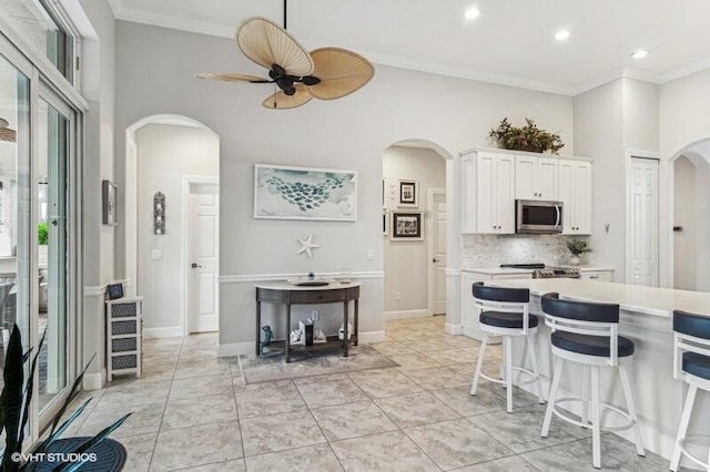 kitchen with light tile patterned flooring, white cabinetry, decorative backsplash, ceiling fan, and crown molding